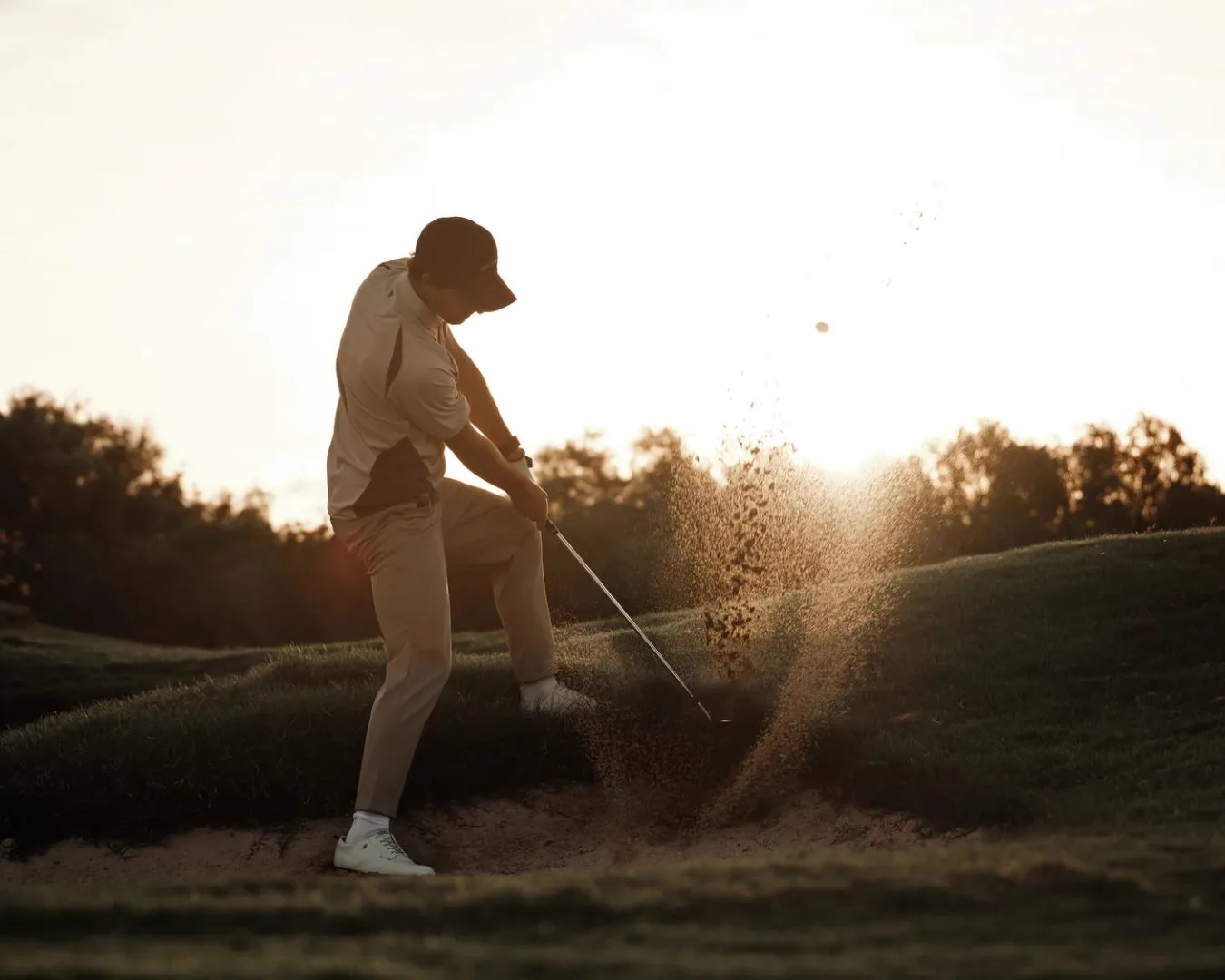 Golfer hitting from sand bunker at sunset